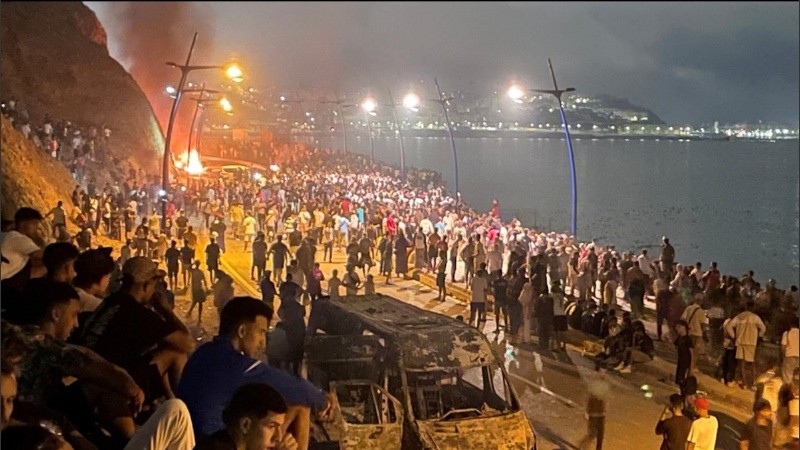 Migrantes reunidos alrededor de un vehículo incendiado mientras esperan la oportunidad de cruzar al enclave español de Ceuta.